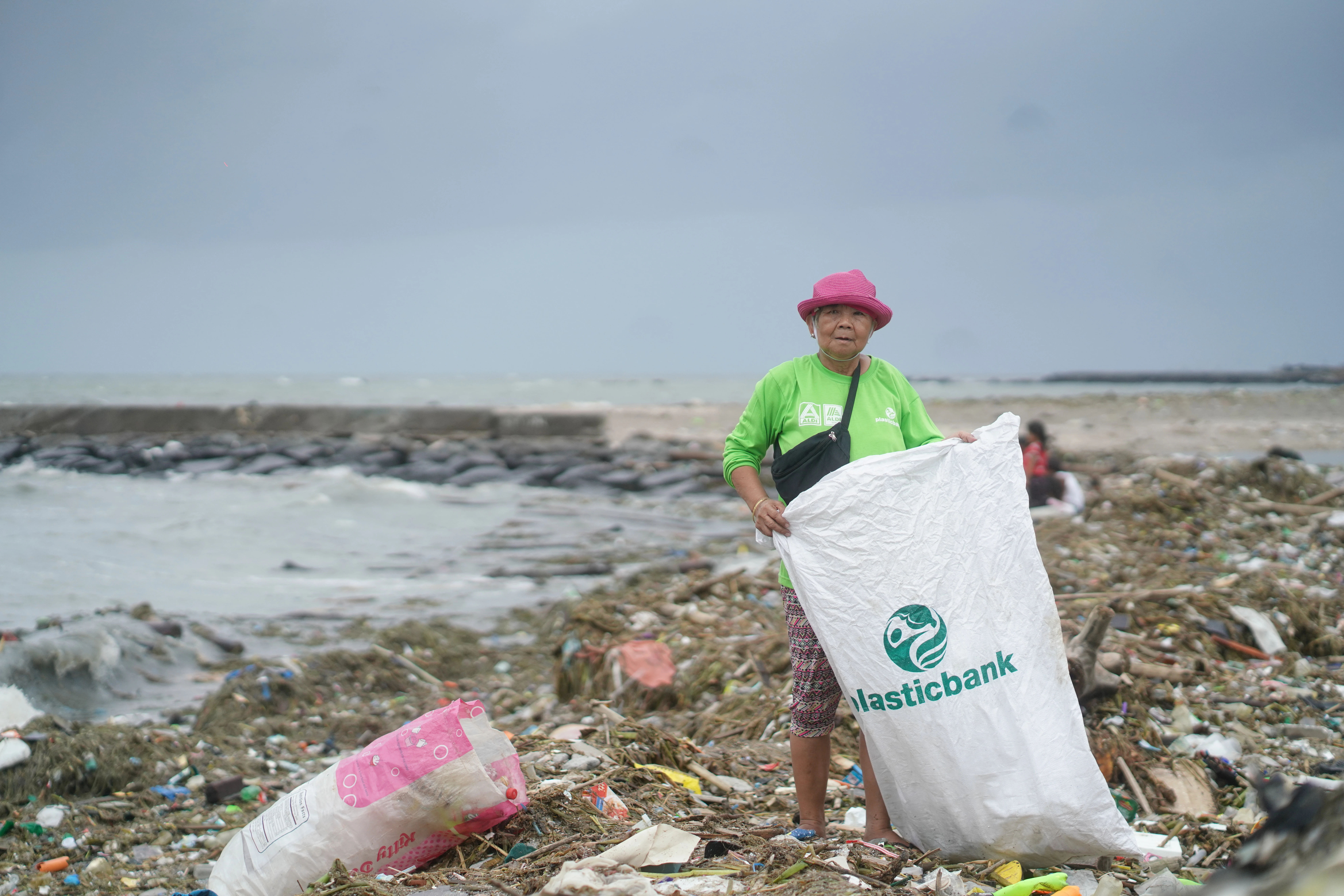 Elizabeth Ampuyas is shown holding a “Plastic Bank” bag on a beach with visible pollution.