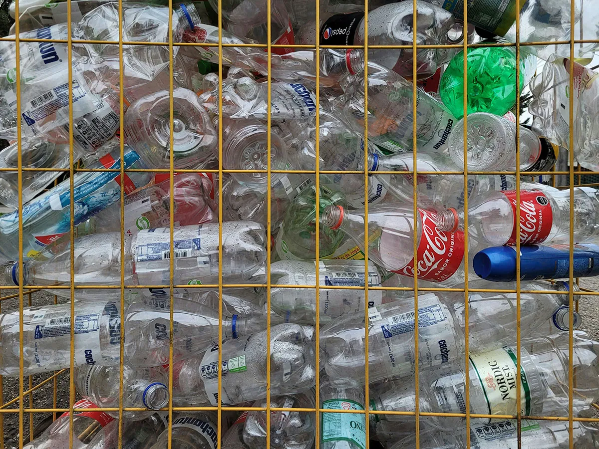  Used plastic bottles and cans packed tightly in a yellow wire basket, ready for recycling.
